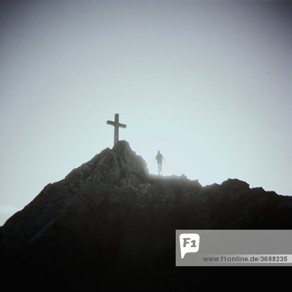A person standing below a crucifix on a mountain top  Mount Saint Michel  Normandy  France