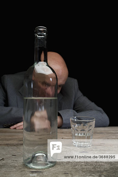 Ein betrunkener und depressiver Geschäftsmann mit einer Flasche Wodka und einem leeren Glas.