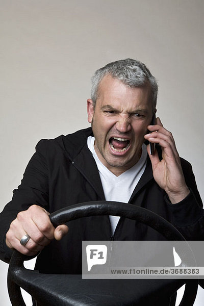 Ein wütender Mann  der ein Handy hinter dem Lenkrad eines Autos benutzt.