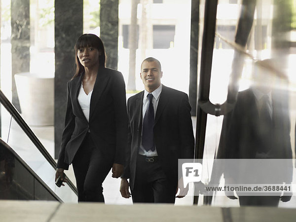 A businesswoman and businessman walking up stairs in an office building