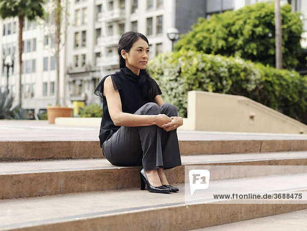 Eine kontemplative Geschäftsfrau sitzt auf der Außentreppe eines Bürokomplexes.