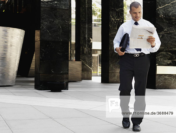 A smiling businessman walking and reading the newspaper