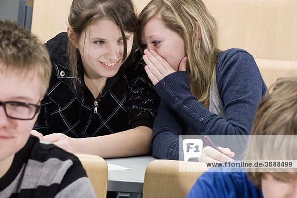 Two female high school students whispering in class