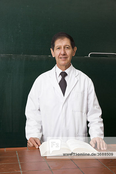 Porträt eines Naturwissenschaftslehrers mit offenem Lehrbuch im Klassenzimmer