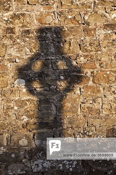 Schatten eines Kreuzes auf einer Steinmauer