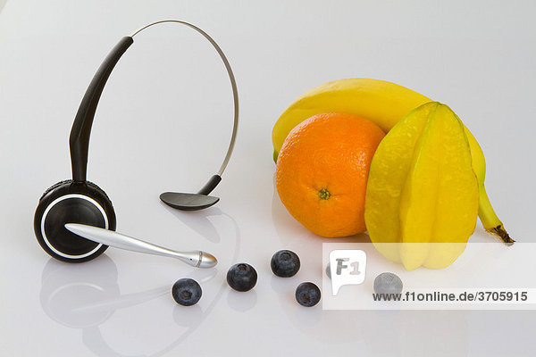 Headphone mit Clementine  Sternfrucht oder Karambole  Banane und Heidelbeeren als Symbol für gesunde Ernährung am Arbeitsplatz