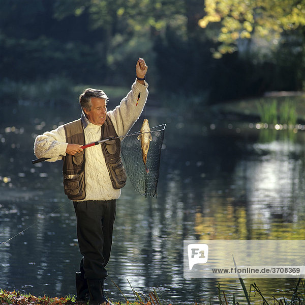 Älterer Angler an einem Teich mit Fisch im Netz
