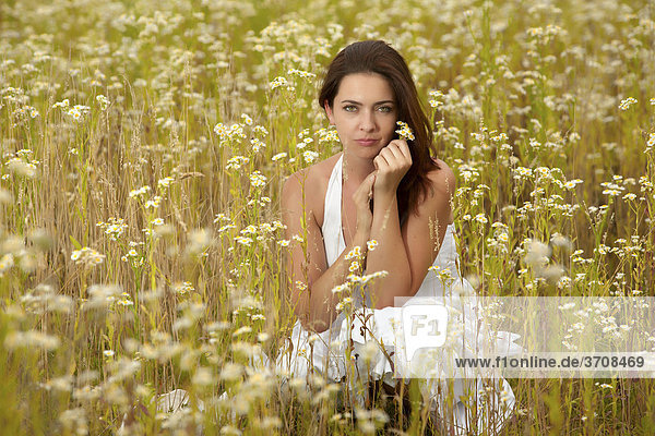 Junge Frau in weißem Kleid im Feld mit Kamillenblüten