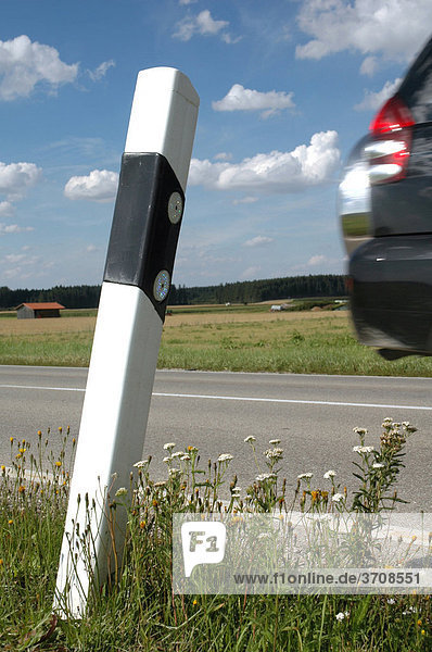 Straßenpfosten am Rande einer Landstraße mit Detail eines vorbeifahrenden Fahrzeugs