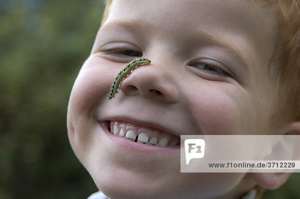 Kind mit einer Raupe im Gesicht Naturentdeckung Naturspiele