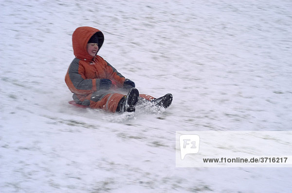 Fünfjähriger Junge rutscht einen Schneehang hununter