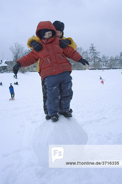 Two boys balancing on big snow ball