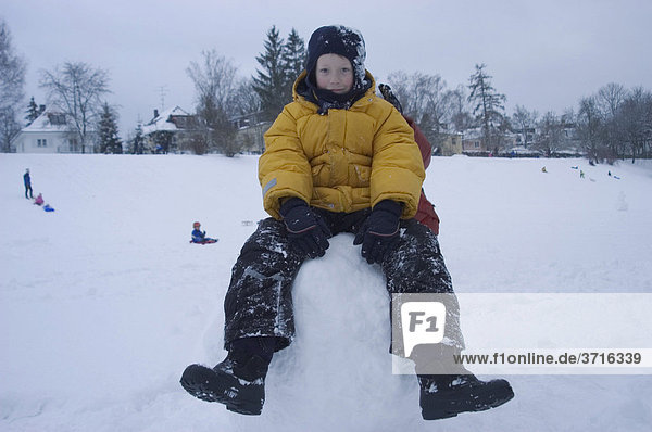 Boy sitting on big snow ball