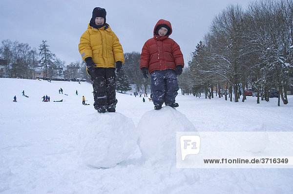 Two boys standing on big snoww balls