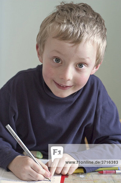 Sechsjähriger Junge sitzt am Schreibtisch beim Hausaufgaben machen