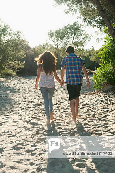 Young couple walking across sand  rear view