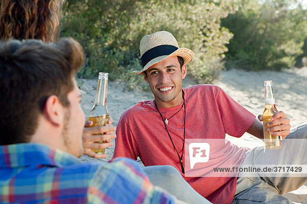 Jungen Freunde sitzen auf Sand mit Bier