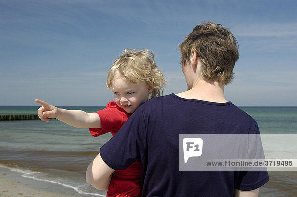 Junge Frau steht am Ostseestrand und hält ihre kleine Tochter auf dem Arm