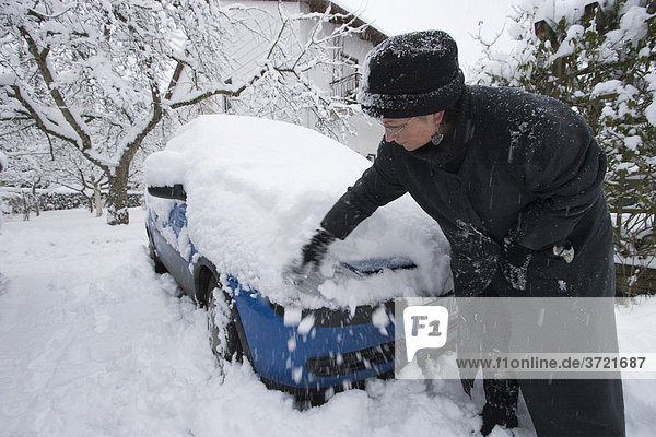 Woman clearing snow off car - snowed up blue car