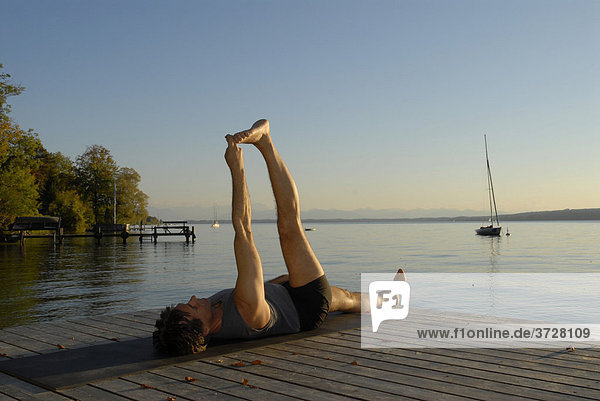 Mann macht Yoga auf Holzsteg am See
