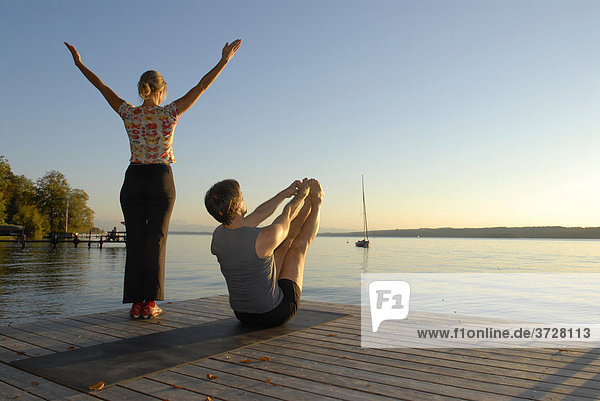 Frau und Mann machen Yoga auf Holzsteg am See