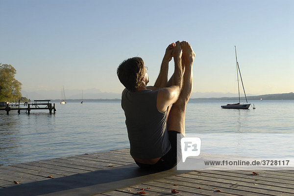 Man doing yoga on a wooden pier by a lake