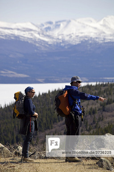 Group of hikers  man and woman hiking  backpacks  ice covered Kusawa Lake behind  Yukon Territory  Canada  North America