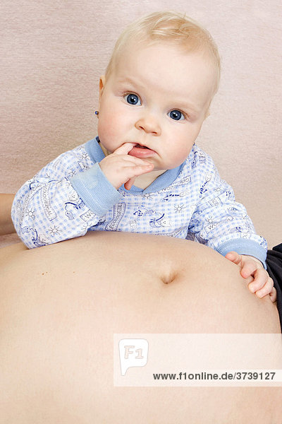 Baby  7 Monate  mit dem Bauch der schwangeren Mutter