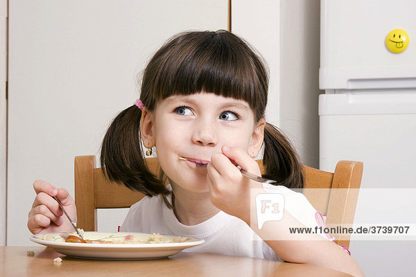 Sechsjähriges Mädchen isst mit Messer und Gabel von einem Teller