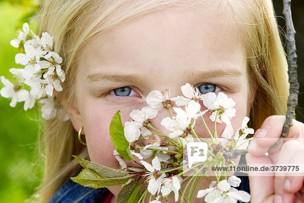 Portrait eines jungen  blonden Mädchens das Blüten im Haar und in der Hand