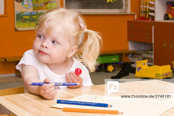 Blond little girl  2 years  with crayons  sitting at table