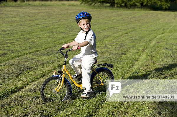 Young boy  4 years old  wearing helmet and riding a bike in a meadow