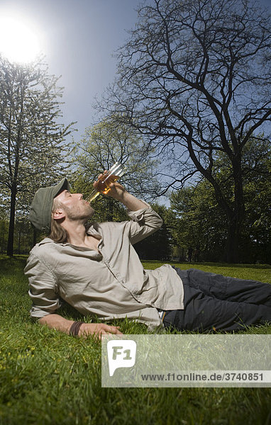 Junger Mann liegt im Park  trinkt