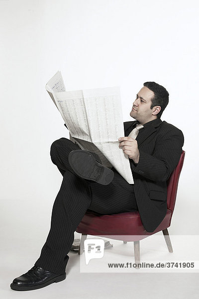 Geschäftsmann liest sitzend in einem roten Sessel seine Zeitung