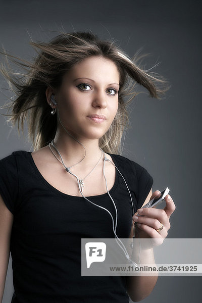 Junge Frau hört Musik mit einem MP3-Player und blickt in Richtung Kamera