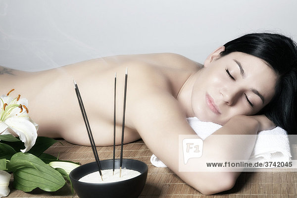 Young woman relaxing while lying on her stomach on a mat next to incense sticks
