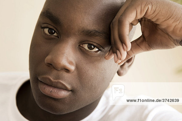 Dark-skinned  15-year-old boy  resting head on hand  pensive