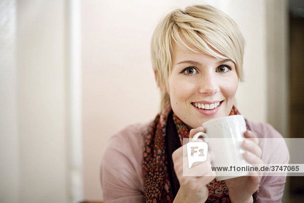 Junge Frau mit kurzen blonden Haaren trinkt Kaffee