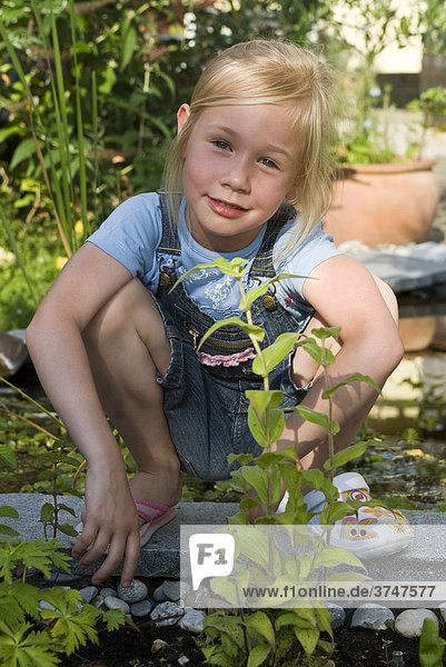 Girl  5  wearing two different shoes  sitting in front of a garden pond
