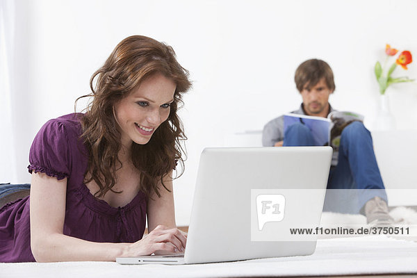 Frau auf dem Laptop  während der Mann liest