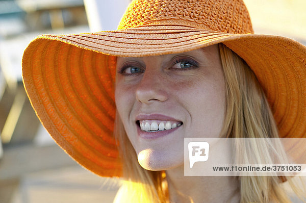 Lächelnde junge Frau mit großem orangen Sommerhut