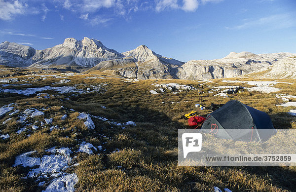 Ein grünes Zelt  gelber Rucksack  rote Daunenjacke und Gaskocher in herbstlicher Berglandschaft  Gröden  Südtirol  Italien  Europa