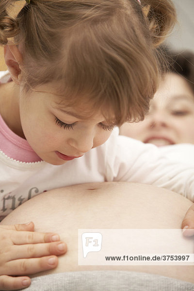 Vierjährige Tochter liebkost den Schwangerschaftbauch ihrer Mutter