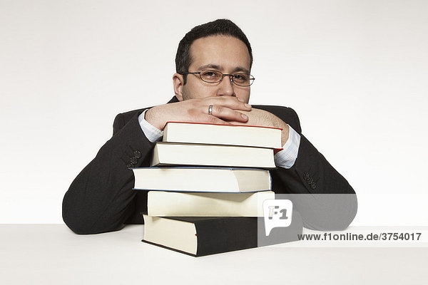 Mann stützt sein Kinn auf Bücherstapel