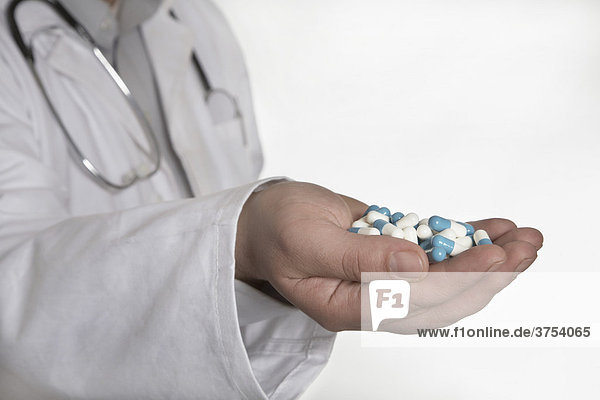 Arzt mit Stetoskop hält eine handvoll Tabletten in Richtung Kamera
