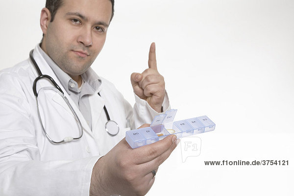 Arzt hält Tablettenbox in Richtung Kamera und hebt mahnend den Finger
