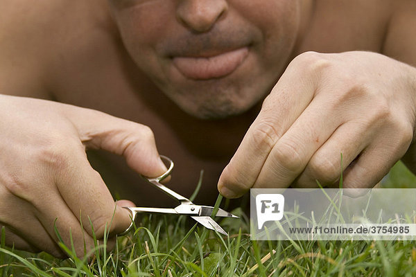 Mann schneidet seinen Rasen mit Nagelschere