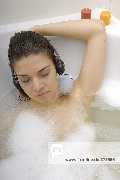Dunkelhaarige Frau in der Badewanne hört Musik mit Kopfhörern