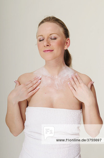 Blonde young woman wrapped in a white towel applying body lotion