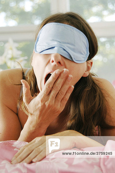 Frau gähnend mit Augenschutz im Bett